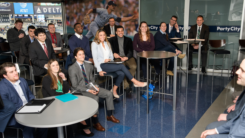 Students gather in a Sports Management class. They're wearing business attire.