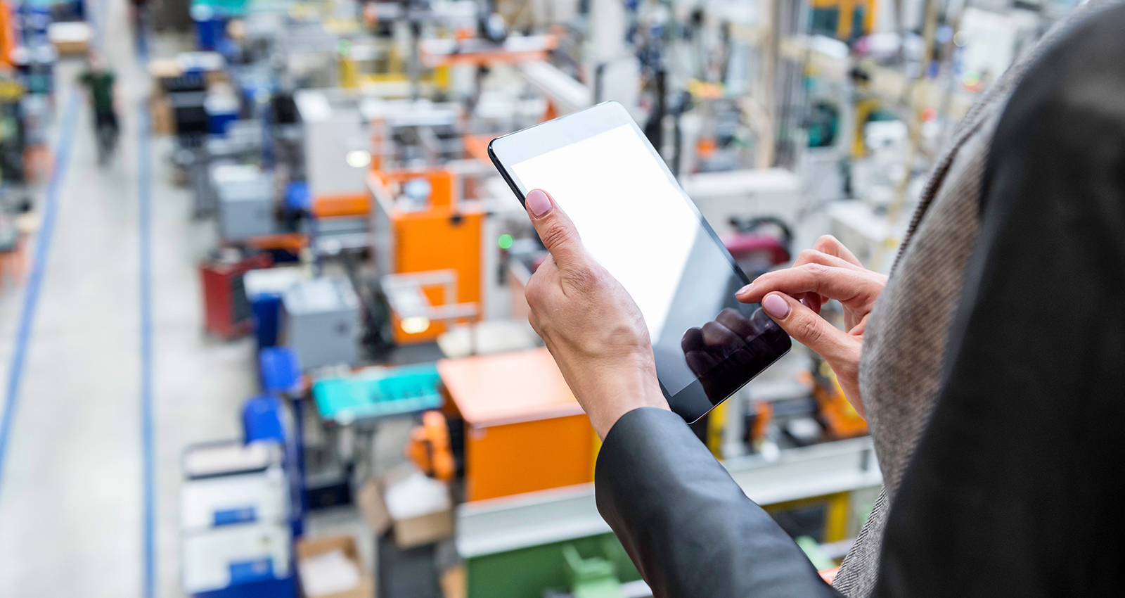 A person standing above a production floor holds a tablet.