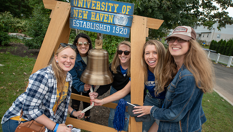 Students pose with the Alumni Bell at Homecoming.