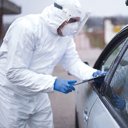 A student in full PPE taking information at a car.