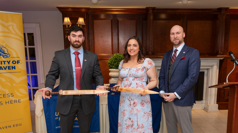 Joshua Wyskiewicz ’25 (left) and Jessica Guglielmo '24 each received a Rudis, a wooden sword with a history extending back to Ancient Rome. Ryan Noonan '20, '23 M.S. is on the right.